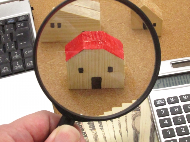 虫眼鏡で赤い屋根の家の模型を見る画像